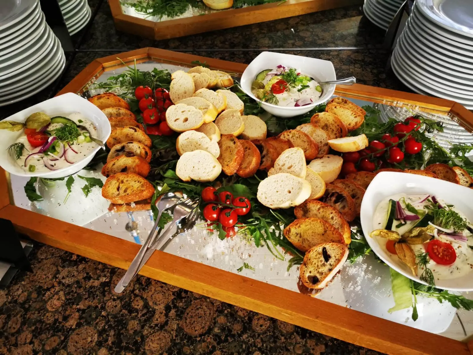 Brotplatte auf Rucola, dazu Dips in weißen Schalen
