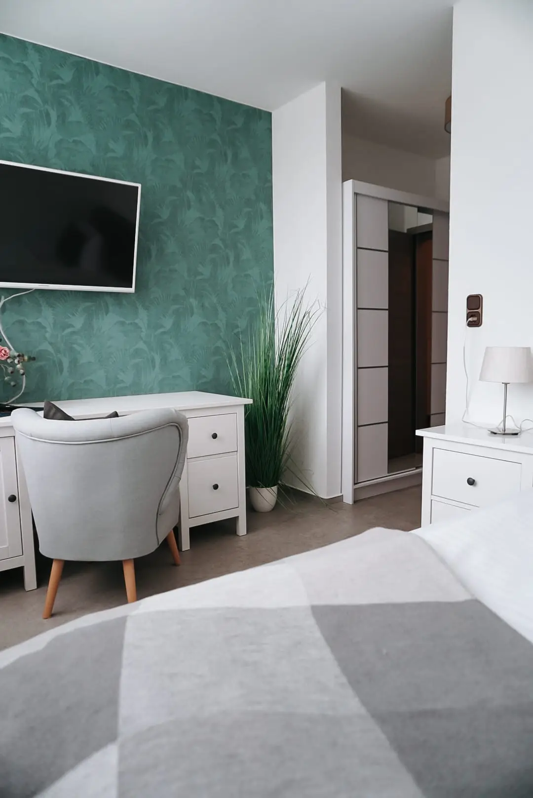 Hotelzimmer mit türkiser Blättertapete, Fernseher und Schreibtisch