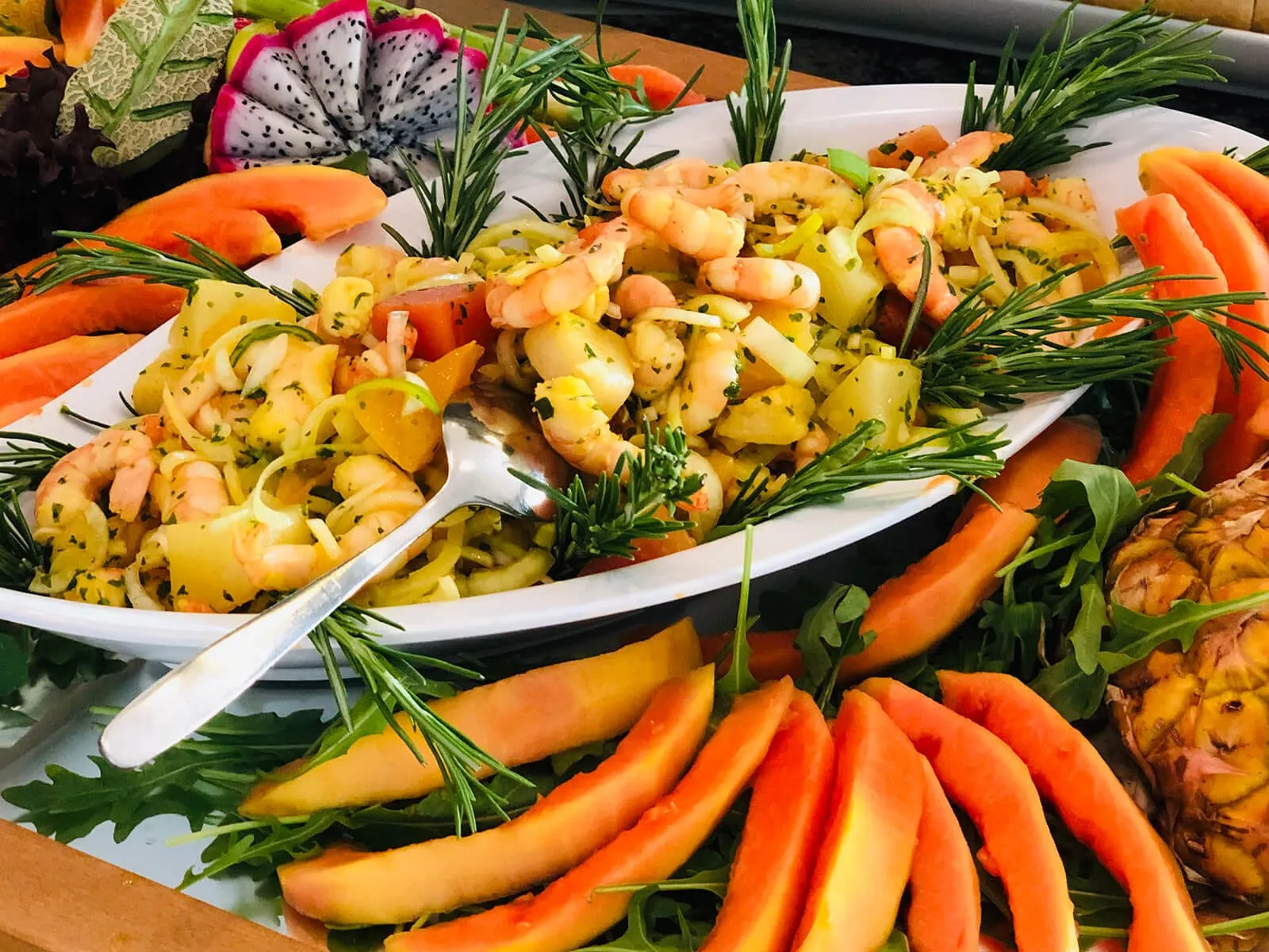 Garnelensalat auf ovaler Platte, umlegt mit Papaya, Melone und Rosmarinzweigen