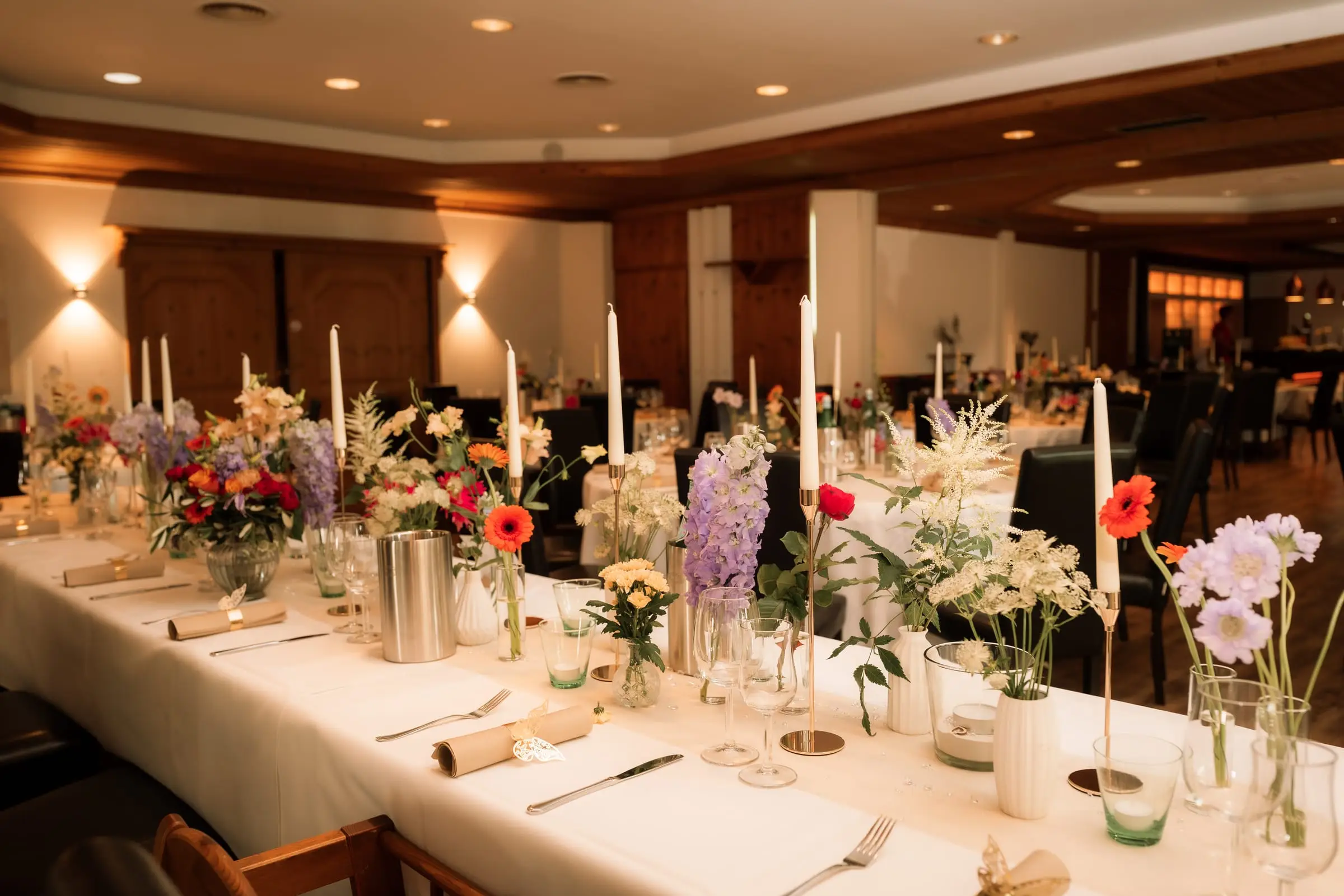 Hochzeitstafel im Saal, mit hohen Kerzen und bunten Blumen