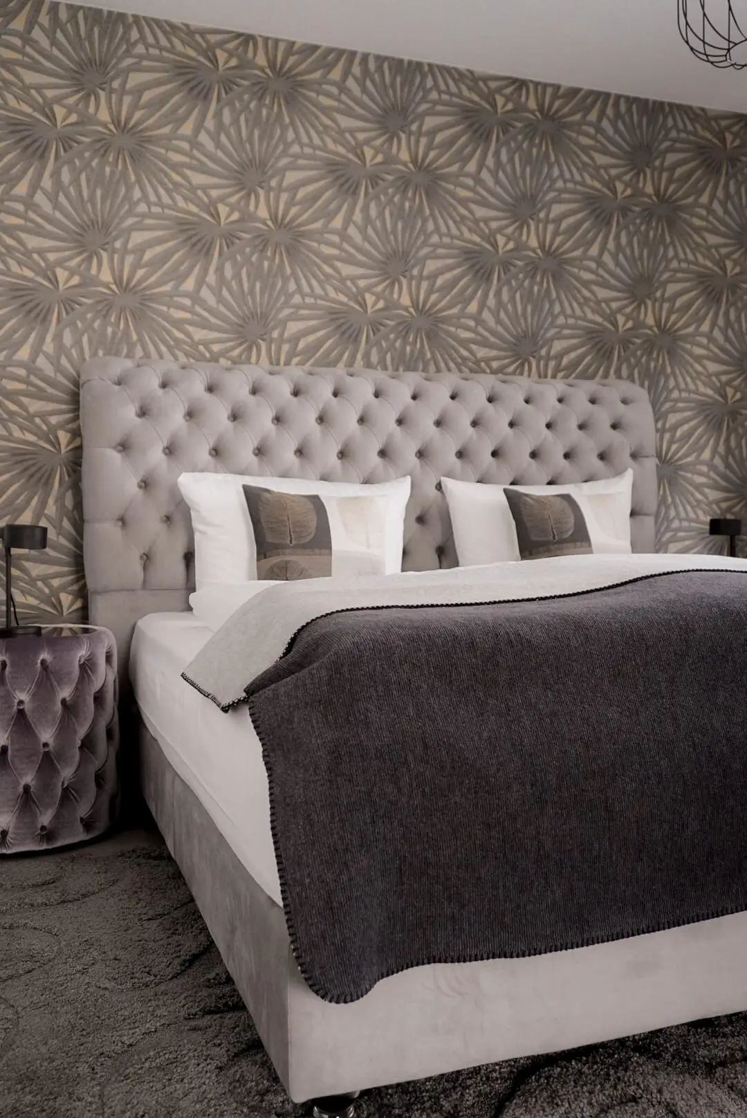 Kingsize-Bett mit hohem Chesterfield-Kopfteil vor grafischer Ornamenttapete