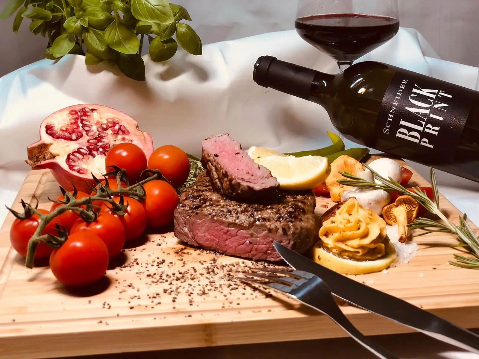 Angeschnittenes Rinderfilet mit Kräuterbutter, Tomaten und Pilzen, dazu ein Glas Rotwein