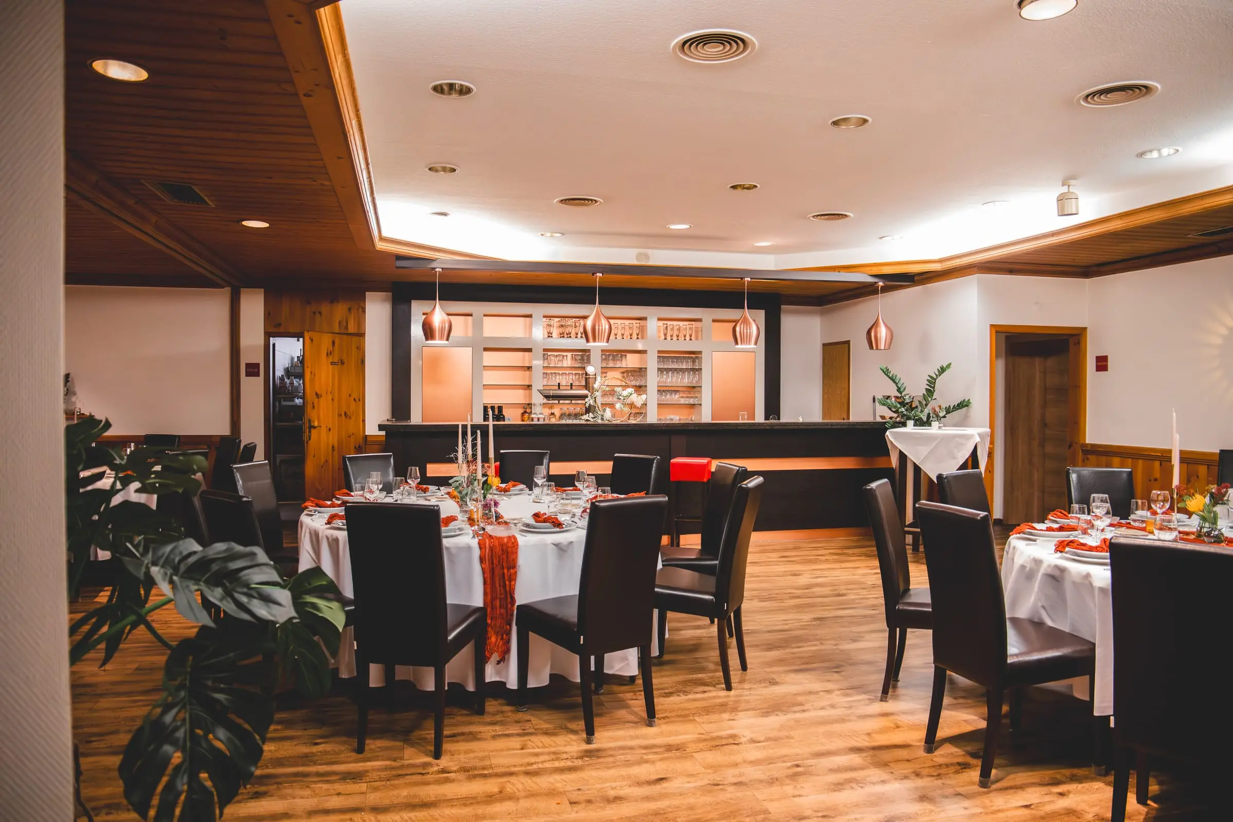 Die Theke im Saal mit Kupferleuchten und Gläserregal, davor eingedeckte Tische