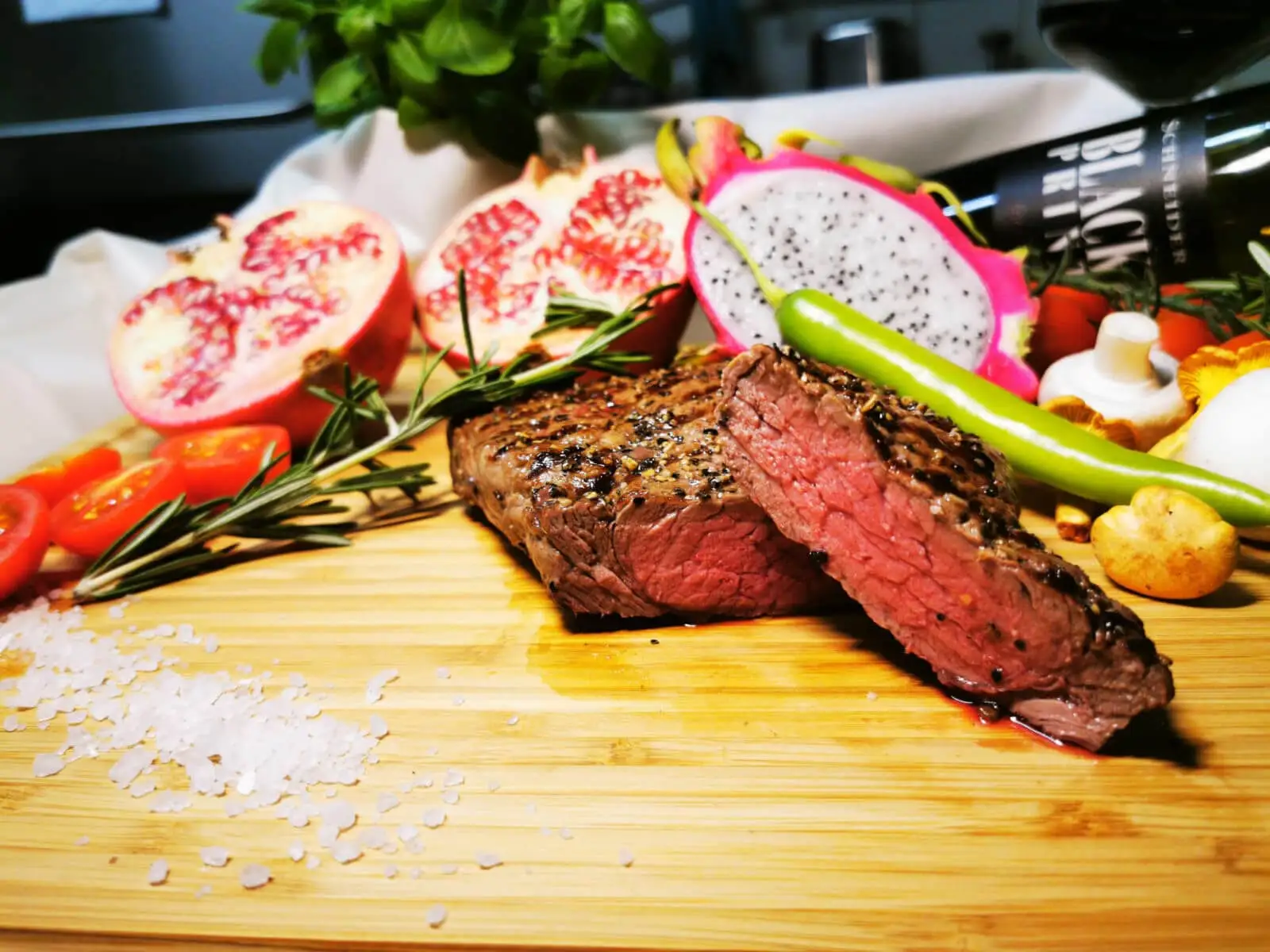 Aufgeschnittenes Steak, rosa gebraten, auf einem Holzbrett mit Feigen und Drachenfrucht
